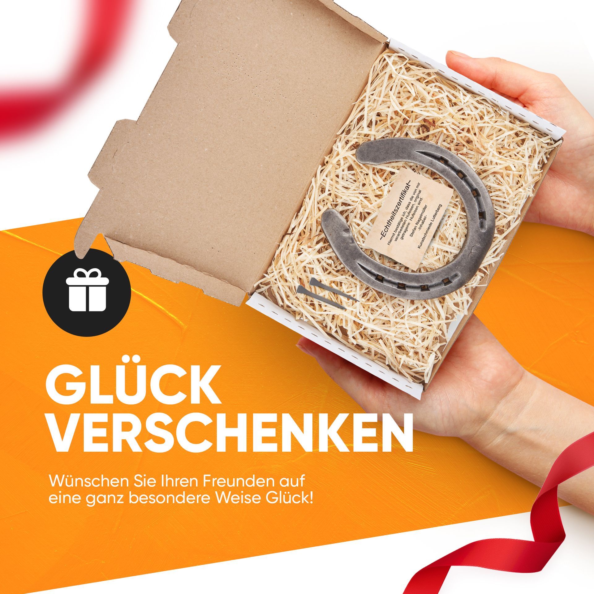 Eine Hand, die einen Schachtel mit Holzwolle und einem Hufeisen und innenliegenden Hufeisennägel , hält. Folgender Text ist zu lesen Glück verschenken Wünschen Sie ihren Freunden auf eine ganz besondere Weise Glück!