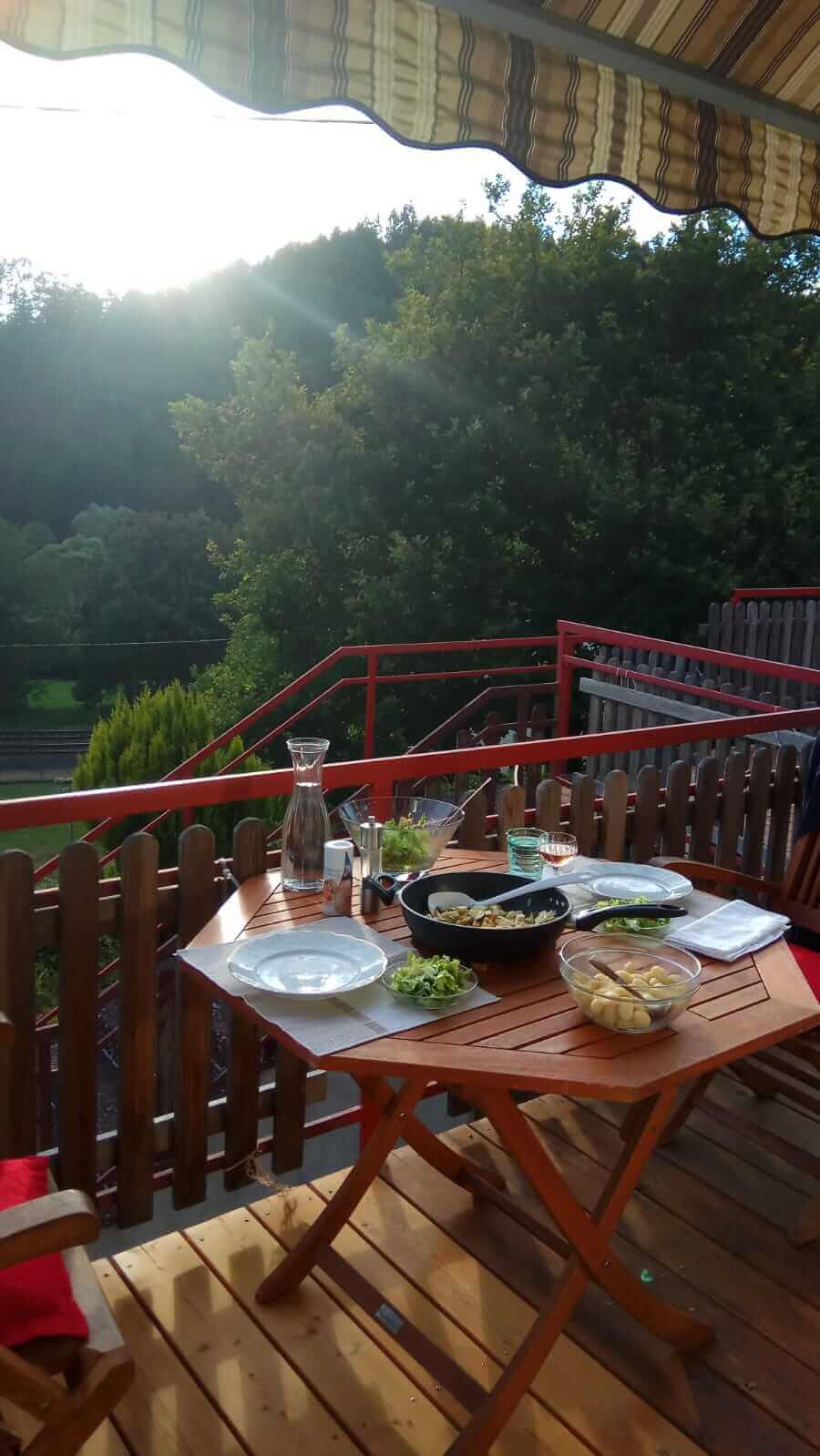 Ernährungsberatung TCM Auf einem Holztisch ist ein Essen angerichtet mit Pfanne, Schüsseln und Tellern. Im Hintergrund viel Natur.