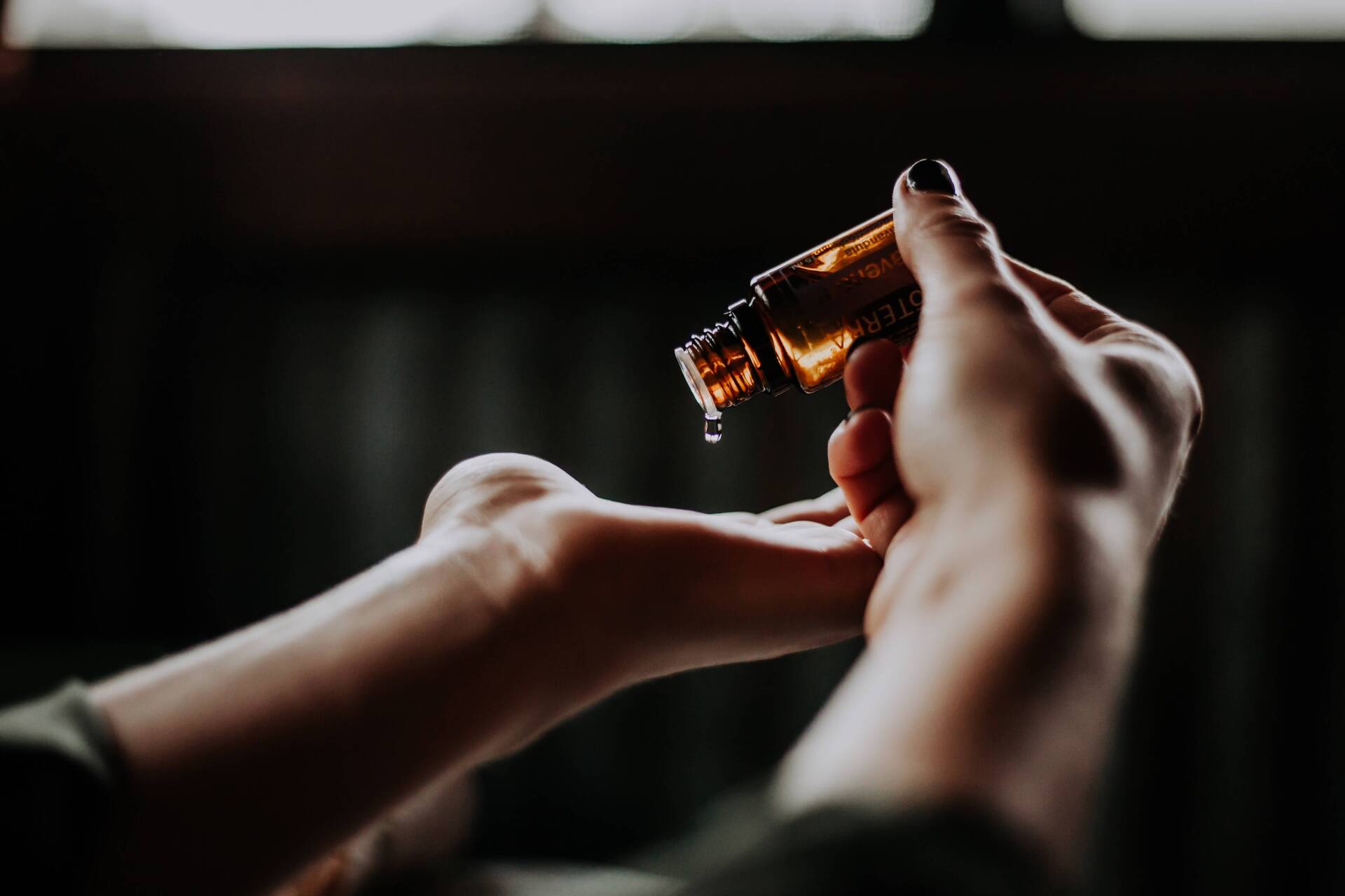 Birgitta Heinz Wellnessmassage Köln Frauenhände vor dunklem Hintergrund. Aromaöl wird in die Handfläche getröpfelt.