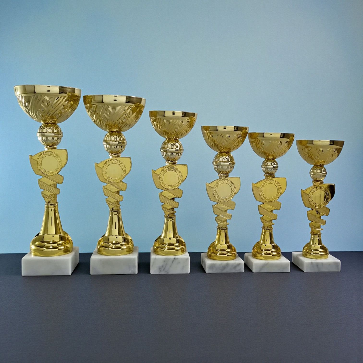 pokale in sechs Größen, goldfarben mit verspieltem Dreh-Design und Marmorfuß – ideal für Nachwuchs-Sportbewerbe.“