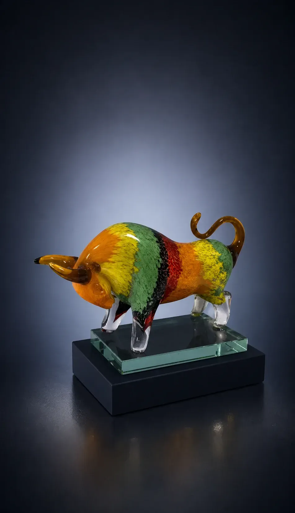 Mehrfarbiger Glasstier in Gelb, Grün, Orange und Rot auf Glasplatte und dunklem Sockel.