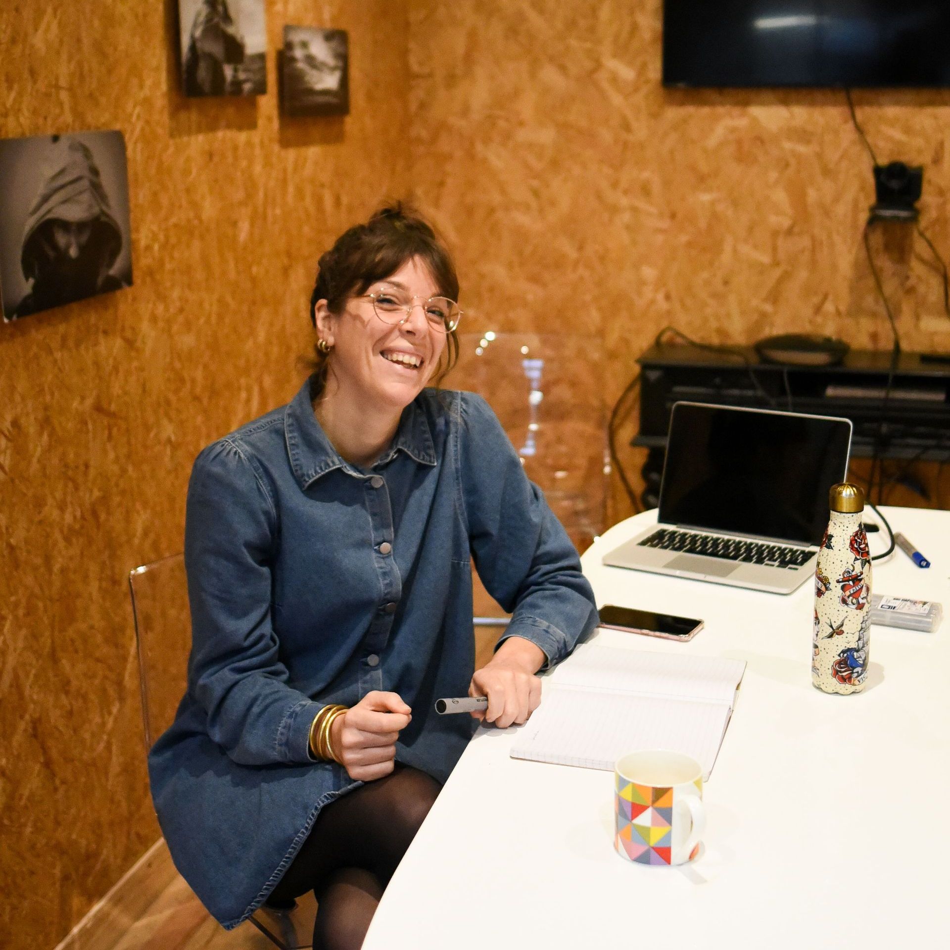 Carole est toute souriante assise à son bureau à la Rochelle. Elle est habillée avec une robe en jean's bleue.