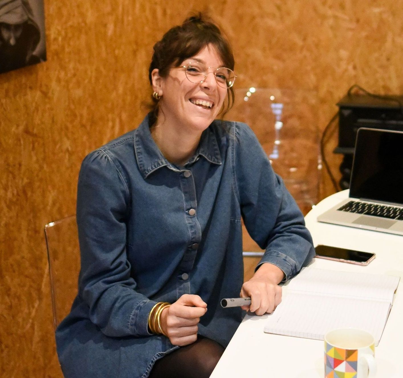 Carole est toute souriante assise à son bureau à la Rochelle. Elle est habillée avec une robe en jean's bleue.