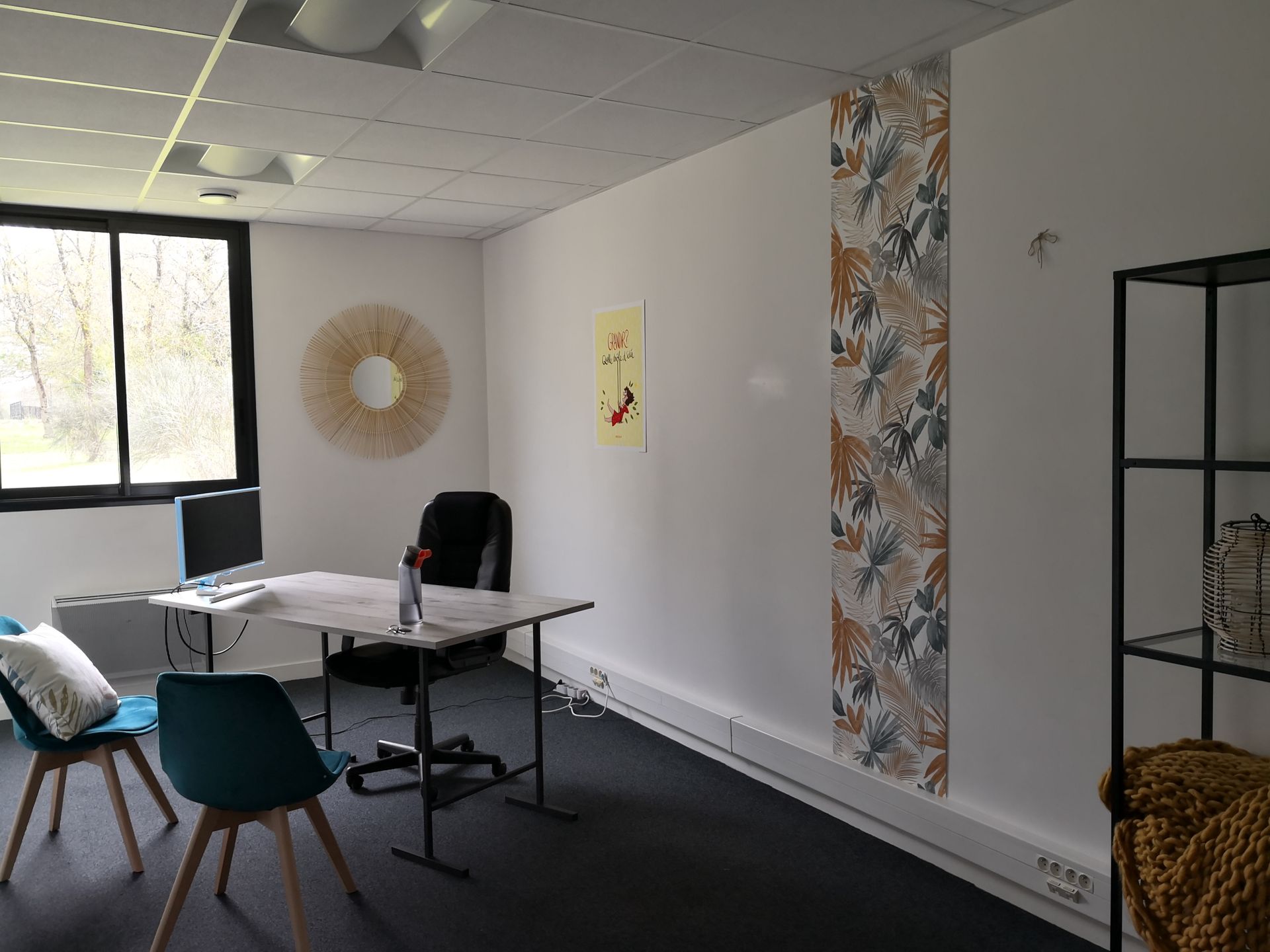 Le bureau de Anne dans les hauts de Couëron. Il est lumineux avec des chaises bleues, un bureau clair. Sur le mur un laie de tapisserie qui donne un coté végétal.