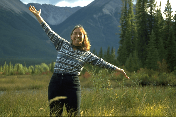 Frau mit offenen Armen mit Bergen und Bäumen im Hintergrund