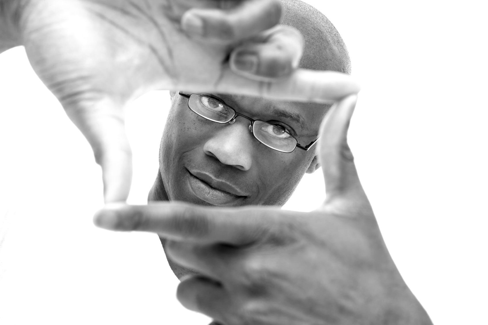 A man looks into the camera through his fingers, which form a rectangle.