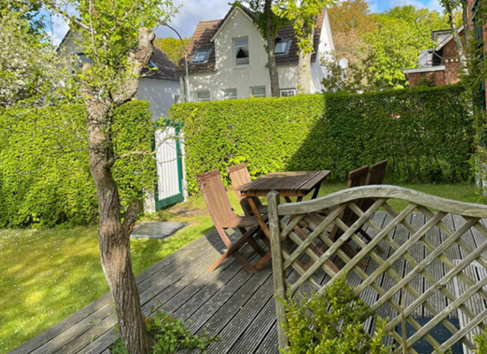 Haus Matthäus Ferienwohnung 1 (EG). Offene Holzterrasse mit Gartenmöbeln. Hohe Hecke als Sichtschutz.