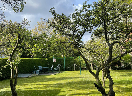 Haus Matthäus Ferienwohnung 2 (OG). Blick durch Obstgarten auf eigene Terrasse mit Gartenmöbeln. Hecke als Sichtschutz.
