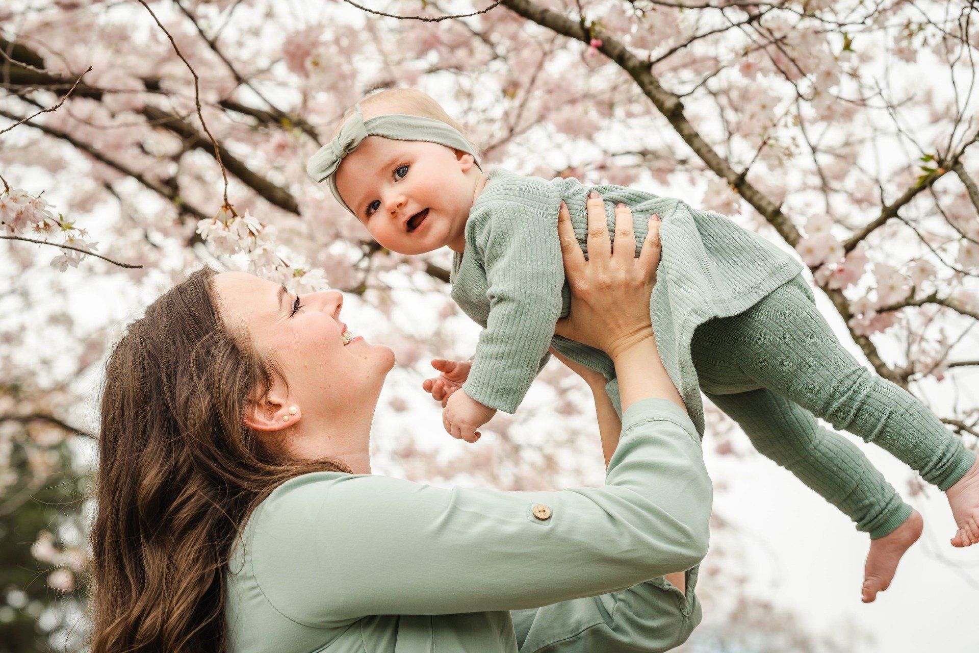 Mutter hebt Baby hoch unter KIrschblütenbaum