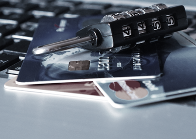 Cajero automático para la retirada de dinero junto a varias tarjetas de crédito y un candado que ha sido desbloqueado, se ve una tarjeta visa y una mastercard.