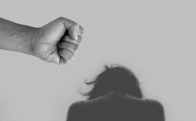 Puño o mano cerrada de un hombre a la izquierda y a la derecha la silueta de una mujer arrodillada con miedo.