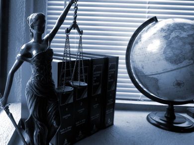Representación del Derecho con varios tomos de derecho penal, un mapa mundi y una escultura que representa la justicia.