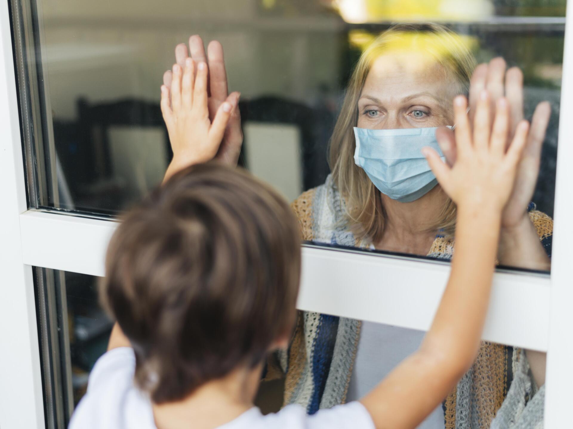 Mujer con mascarilla quirúrgica que saludando a un familiar desde la ventana
