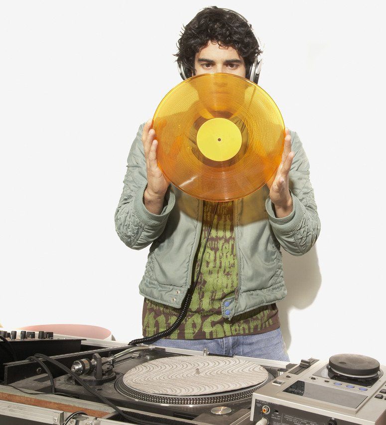 Ein DJ mit Kopfhörern hält eine goldene Schallplatte vor einem Plattenspieler. DJ in Kassel.