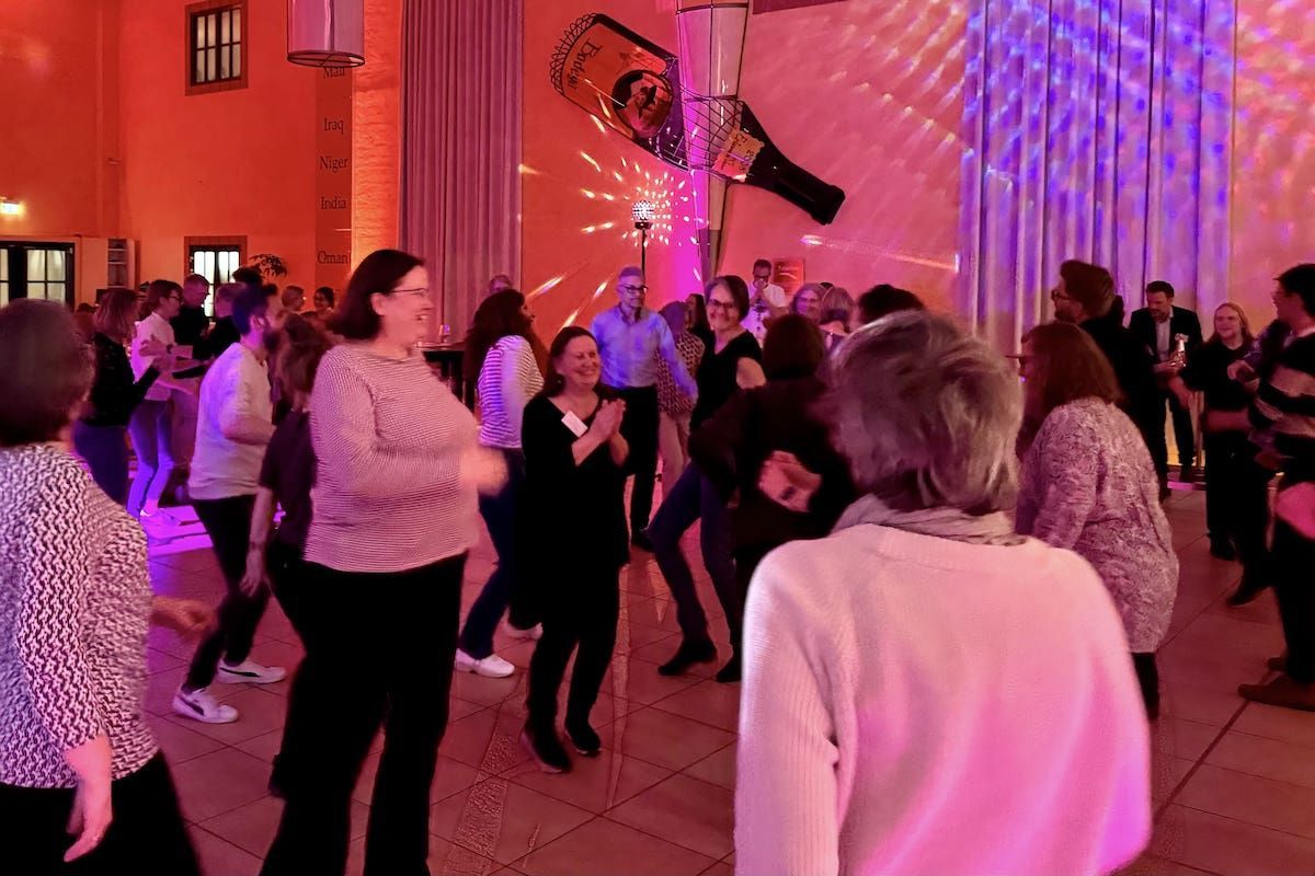 Menschen tanzen auf einer Veranstaltung unter bunten Lichtern.