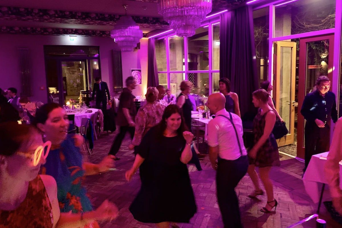 Eine Gruppe von Leuten tanzt ausgelassen auf einer Veranstaltung mit lila Beleuchtung