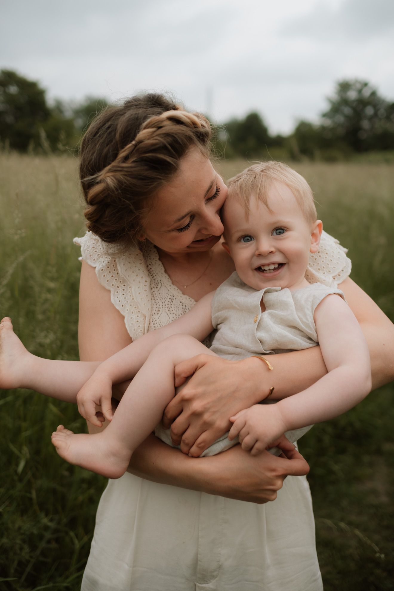Mama hält lächelnden Sohn beim Motherhood Shooting auf einer Wiese in Oberhausen auf dem Arm