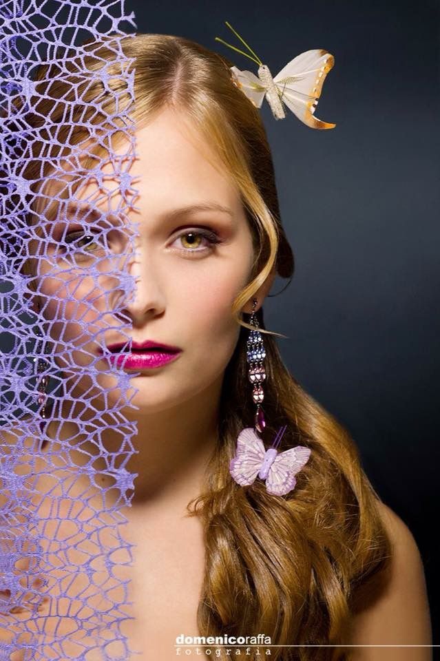 Una donna in primo piano con trucco rosa e un rete viola che le copre metà del viso