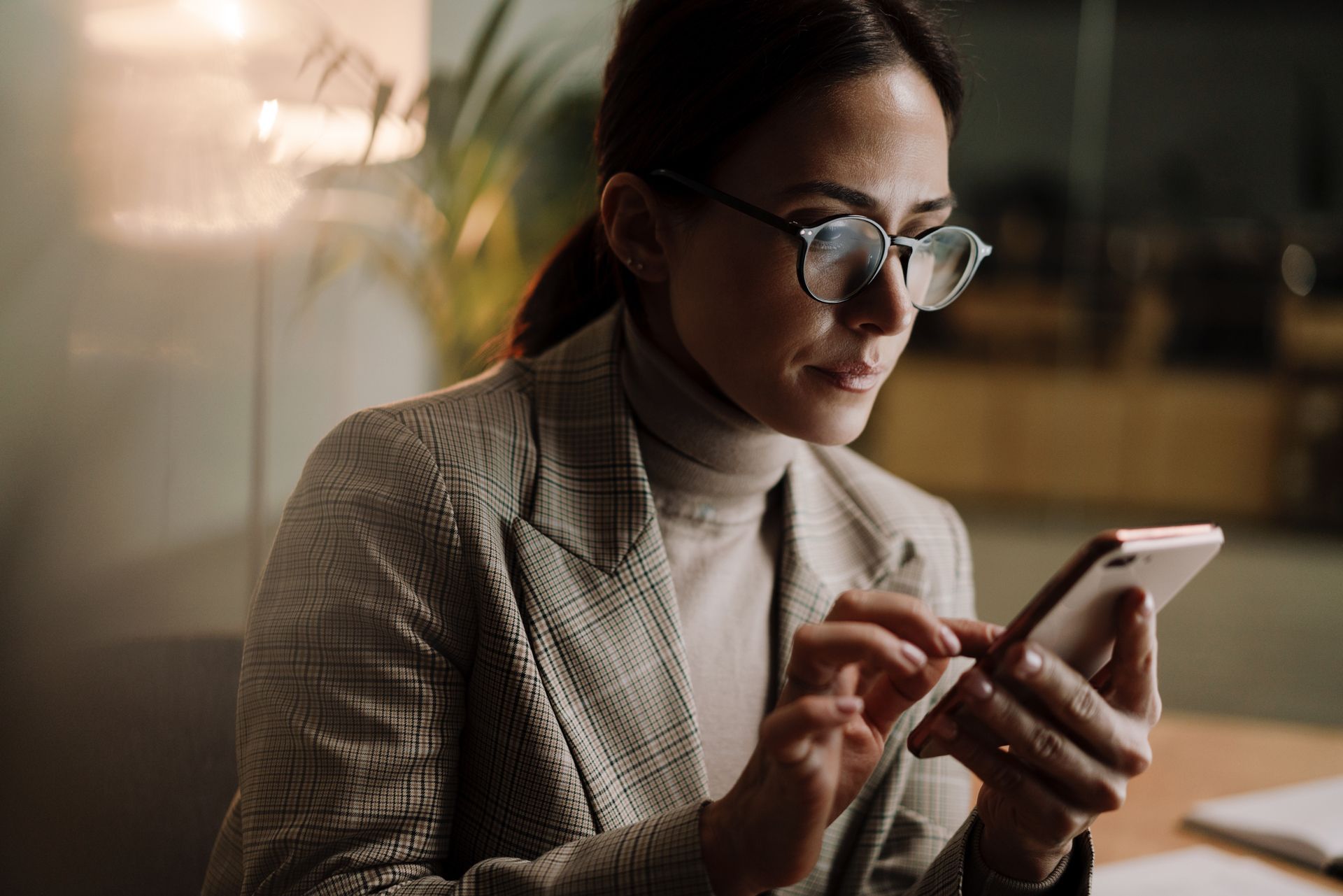 Eine Frau mit Brille schaut in ihr Smartphone. Die Brillengläser zeigen wenige Reflexe des Bildschirms.