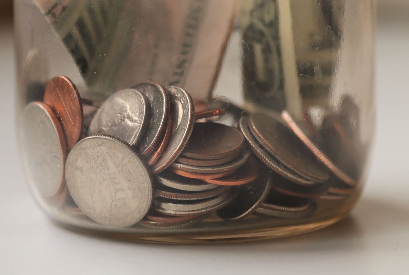 picture of money - change and some dollar bills in the bottom of a glass jar