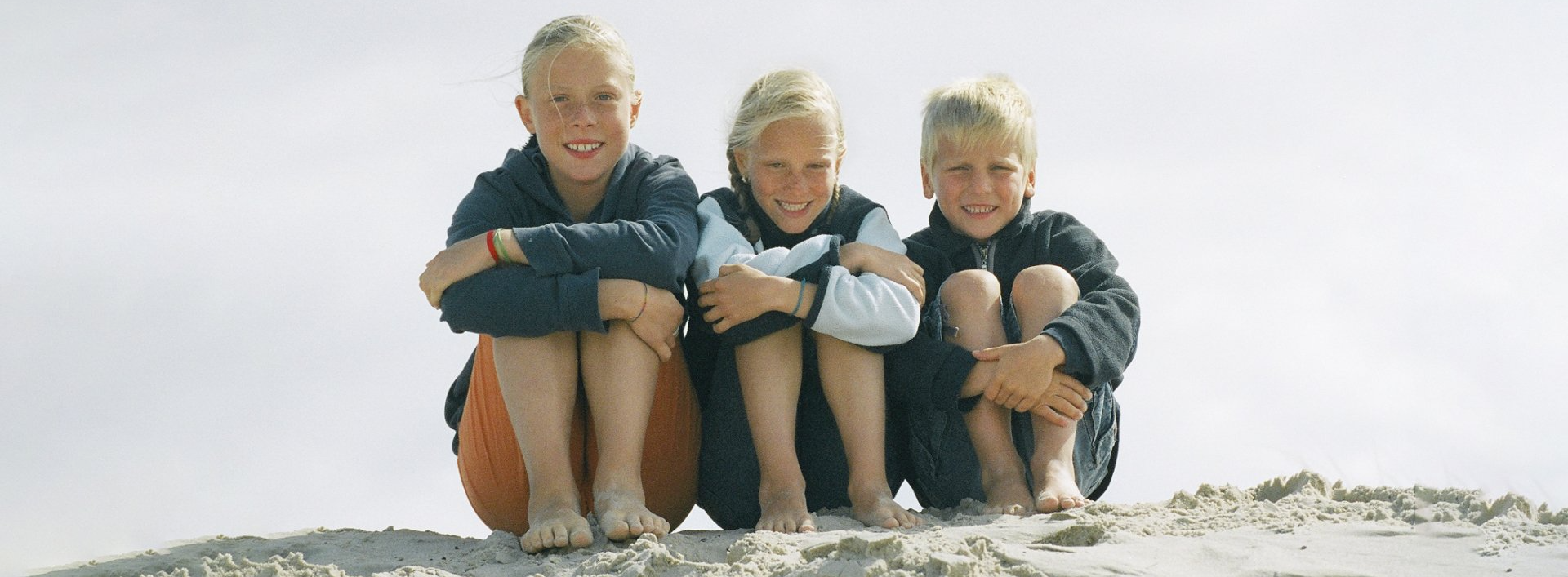 Foto von drei Kindern, die am Strand sitzen