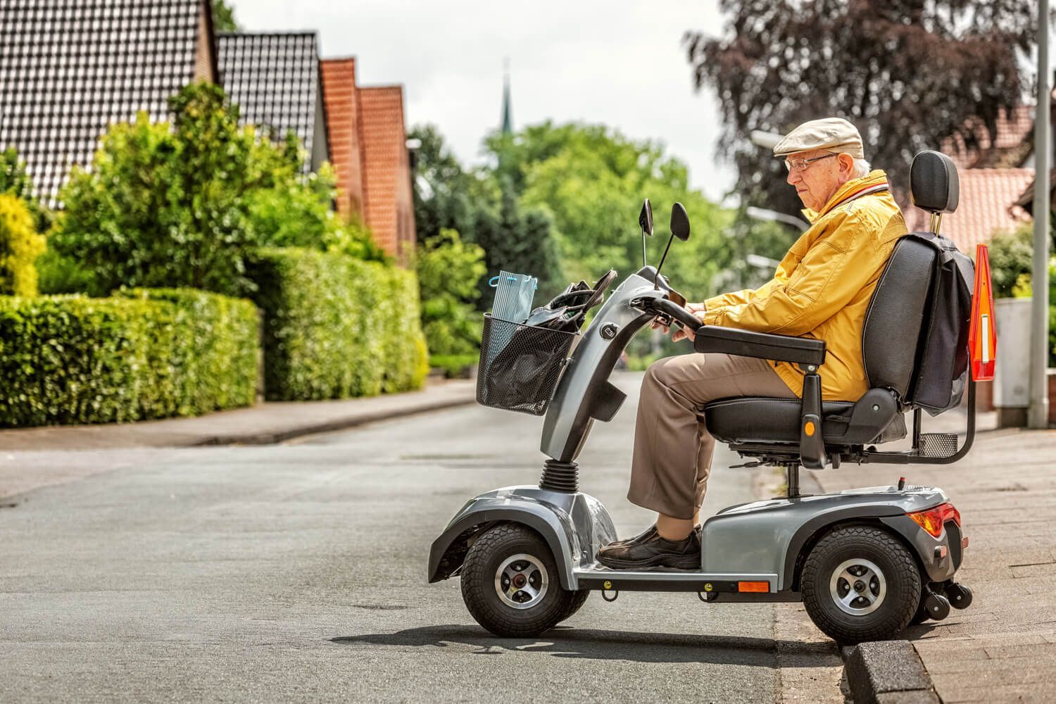 Foto von einem älteren Mann, der in einem Elektroscooter vom Fußweg auf eine kleinere Straße fährt