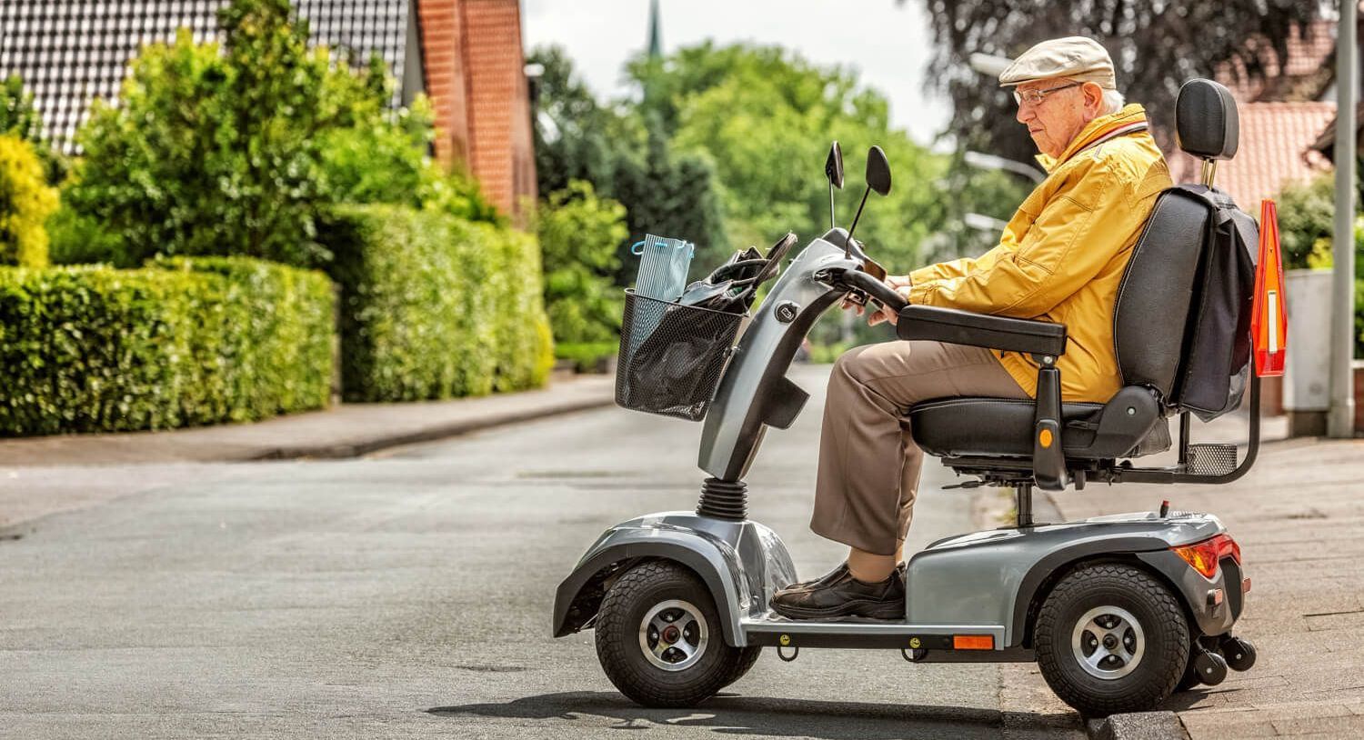Foto von einem älteren Mann, der in einem Elektroscooter vom Fußweg auf eine kleinere Straße fährt Foto von einem älteren Mann, der in einem Elektroscooter vom Fußweg auf eine kleinere Straße fährt