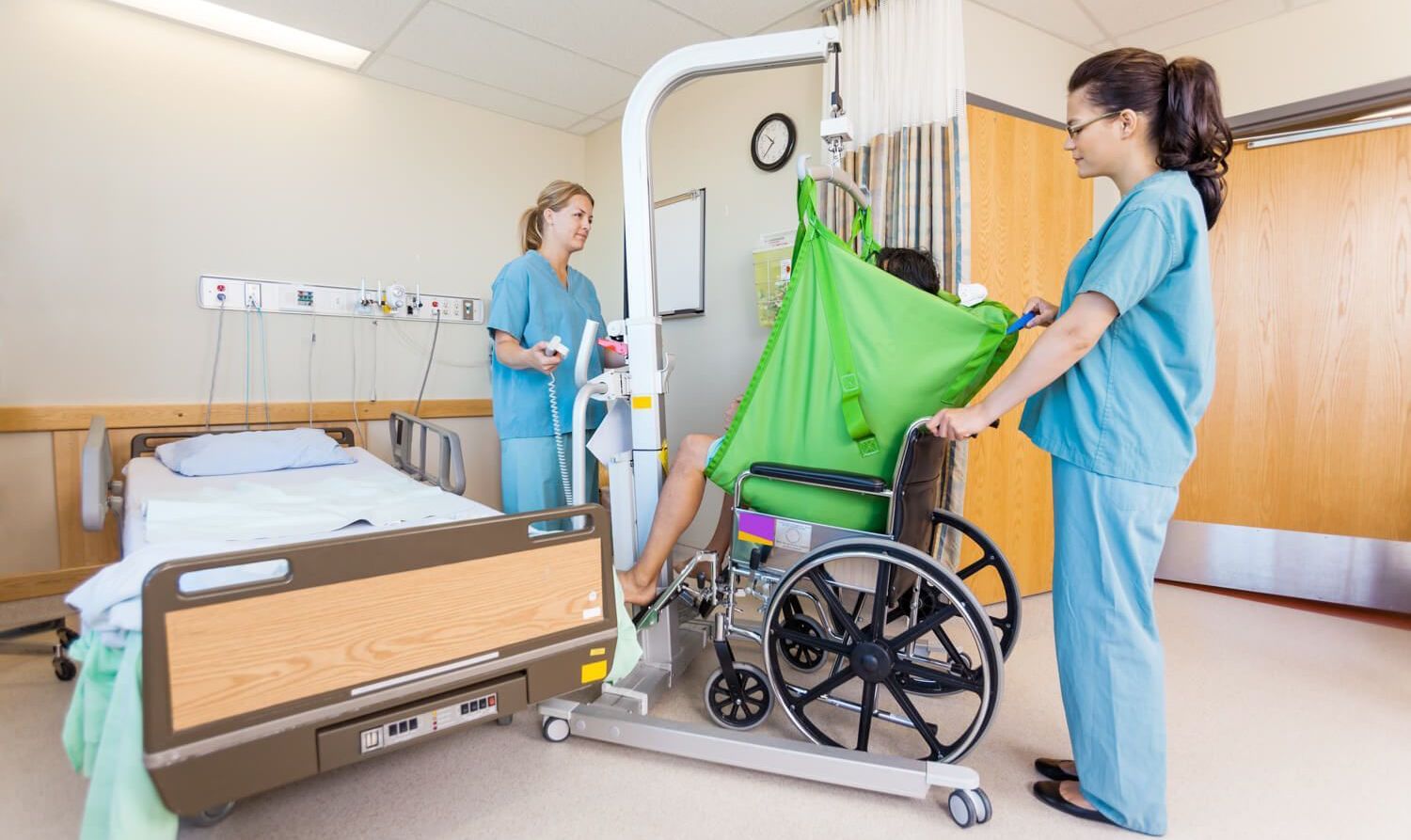 Foto eines Patientenlifts, mit dem in einem Krankenhaus ein Patient aus einem Rollstuhl gehoben wird