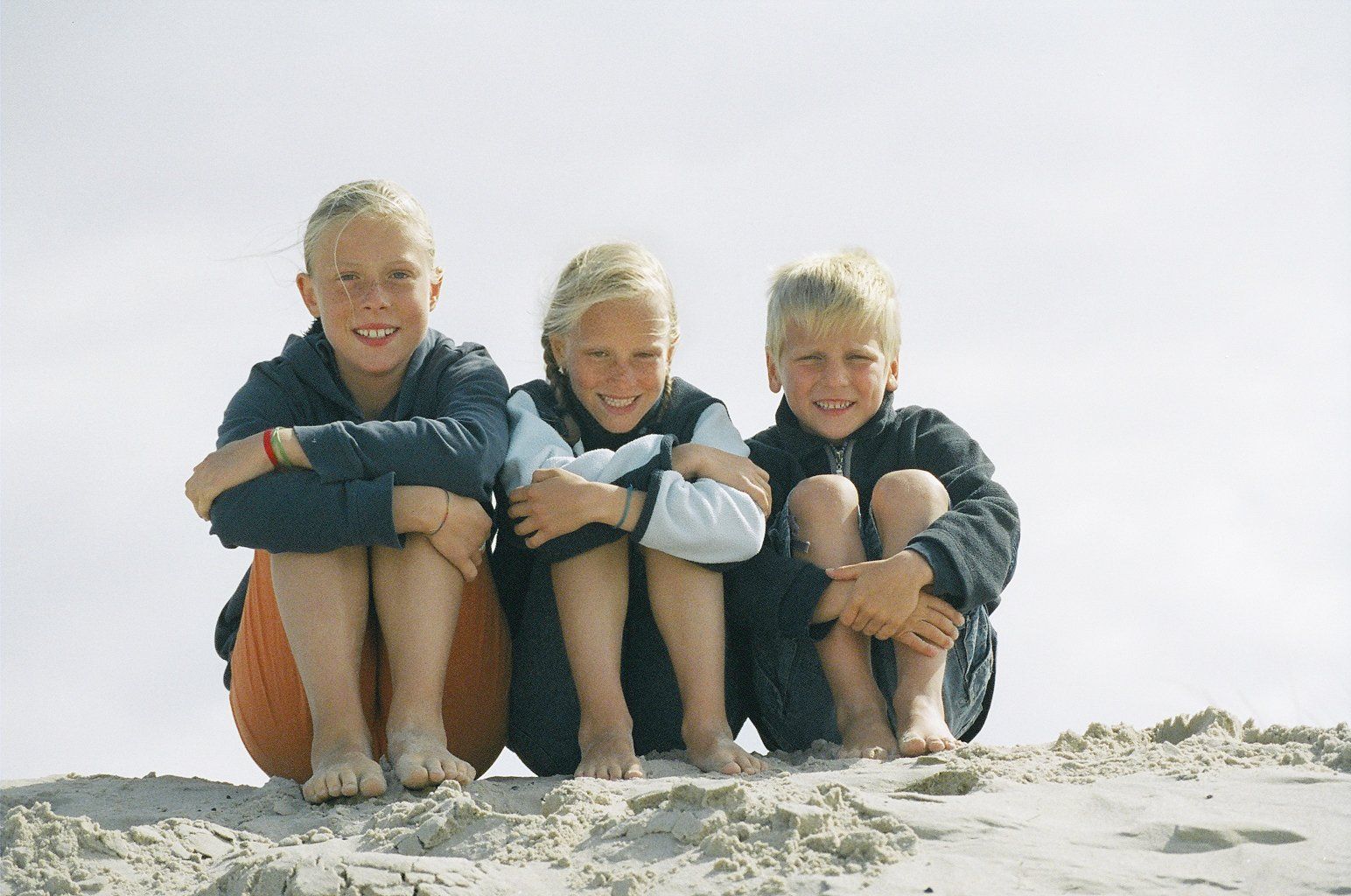 Foto von drei Kindern, die am Strand sitzen