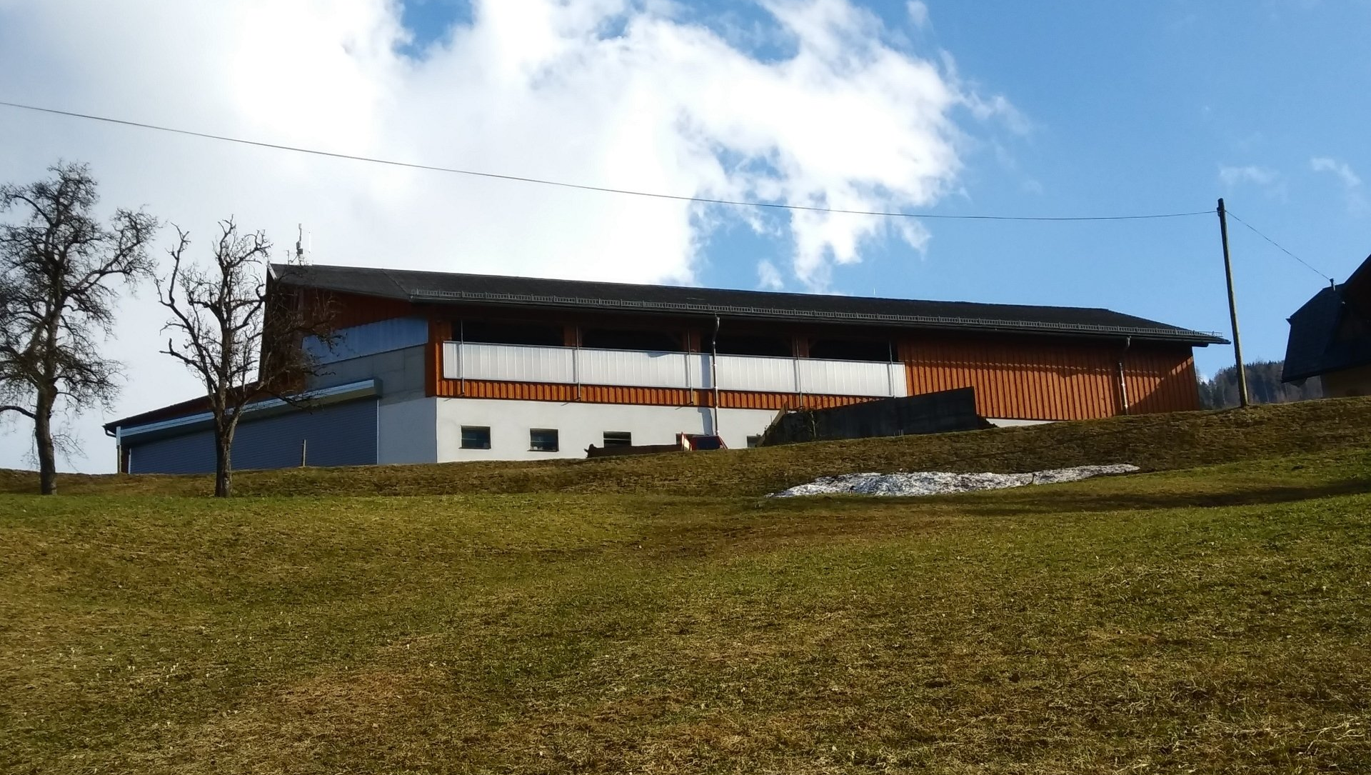 Neubau Mutterkuhstall und Einstellbereich Der Mutterkuhstall ist perfekt in das Gelände gebaut. Das Tretmistsystem bietet den Kühen viel Platz. Mit der Schieberentmistung un dem Heukran, der auf den Futtertisch gelangt, ist der Stall arbeitswirtschaftlich. Im Untergeschoss bietet der Einstellbereich den Maschinen und Geräten Platz zum Einstellen.