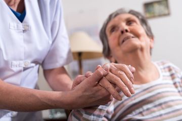 Die Hand einer älteren Dame wird von einer Pflegekraft gehalten
