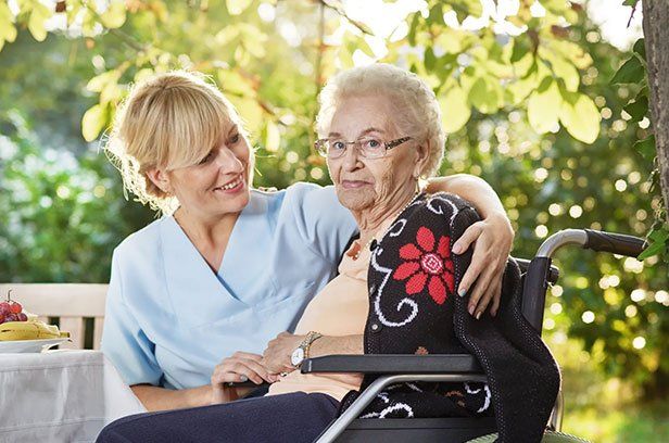 Notfalltraining im Altenheim Eine Pflegerin lächelt eine ältere Dame im Rollstuhl an.