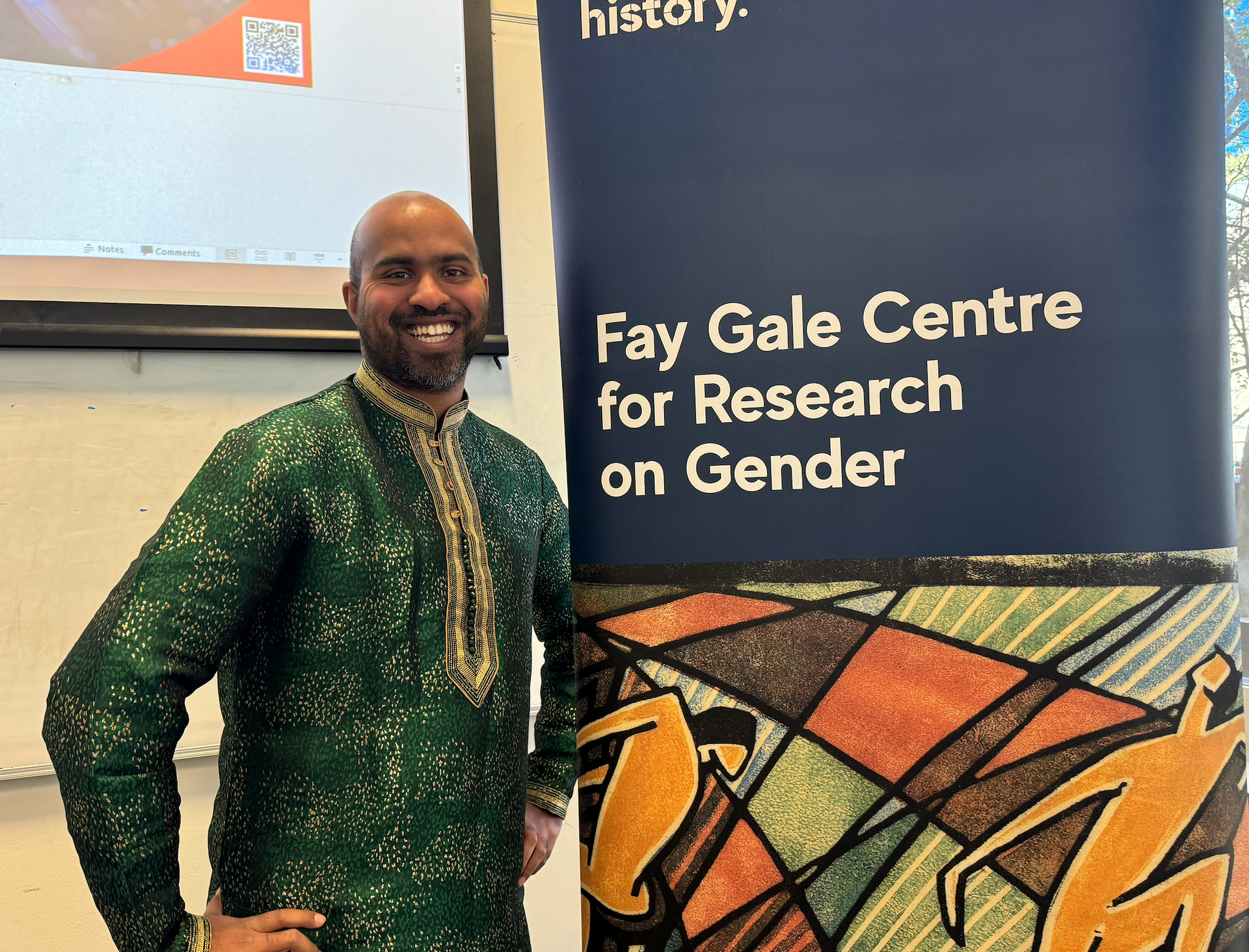 Dr. Dmello in front of a banner for the Fay Gale Centre for Research on Gender