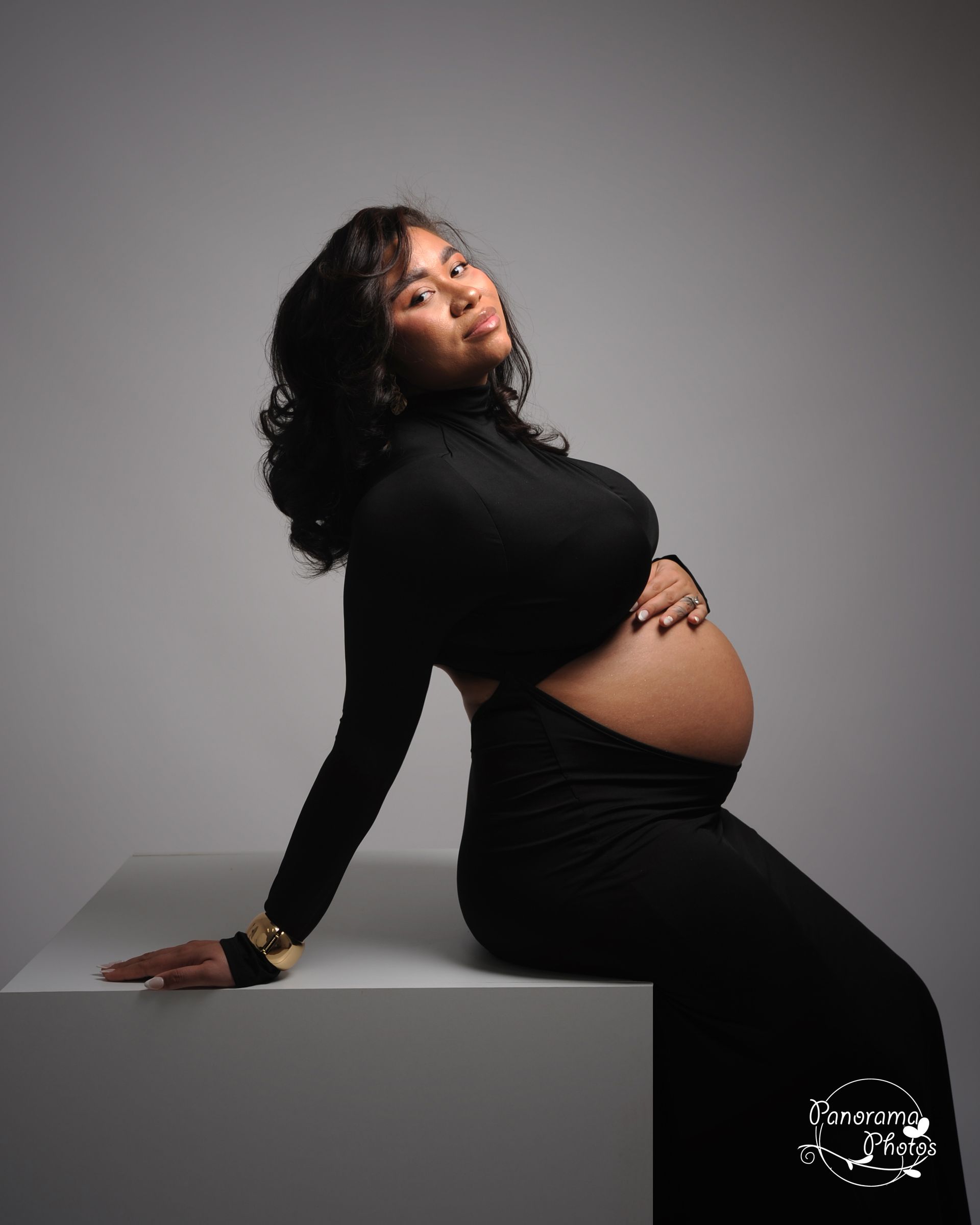 Femme enceinte assise sur un cube blanc avec une robe noire laissant apparaitre son ventre