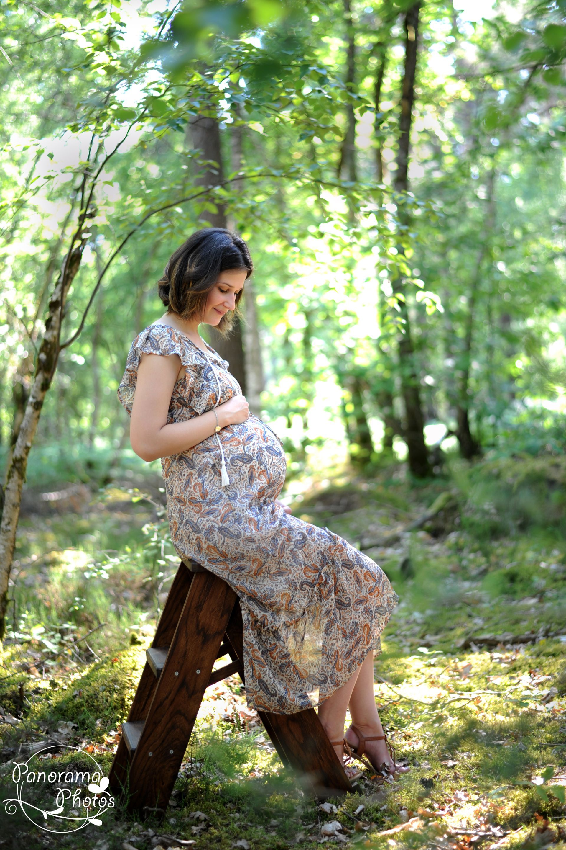 séance photo extérieure portrait femme enceinte assise sur un escabeau en bois dans une foret