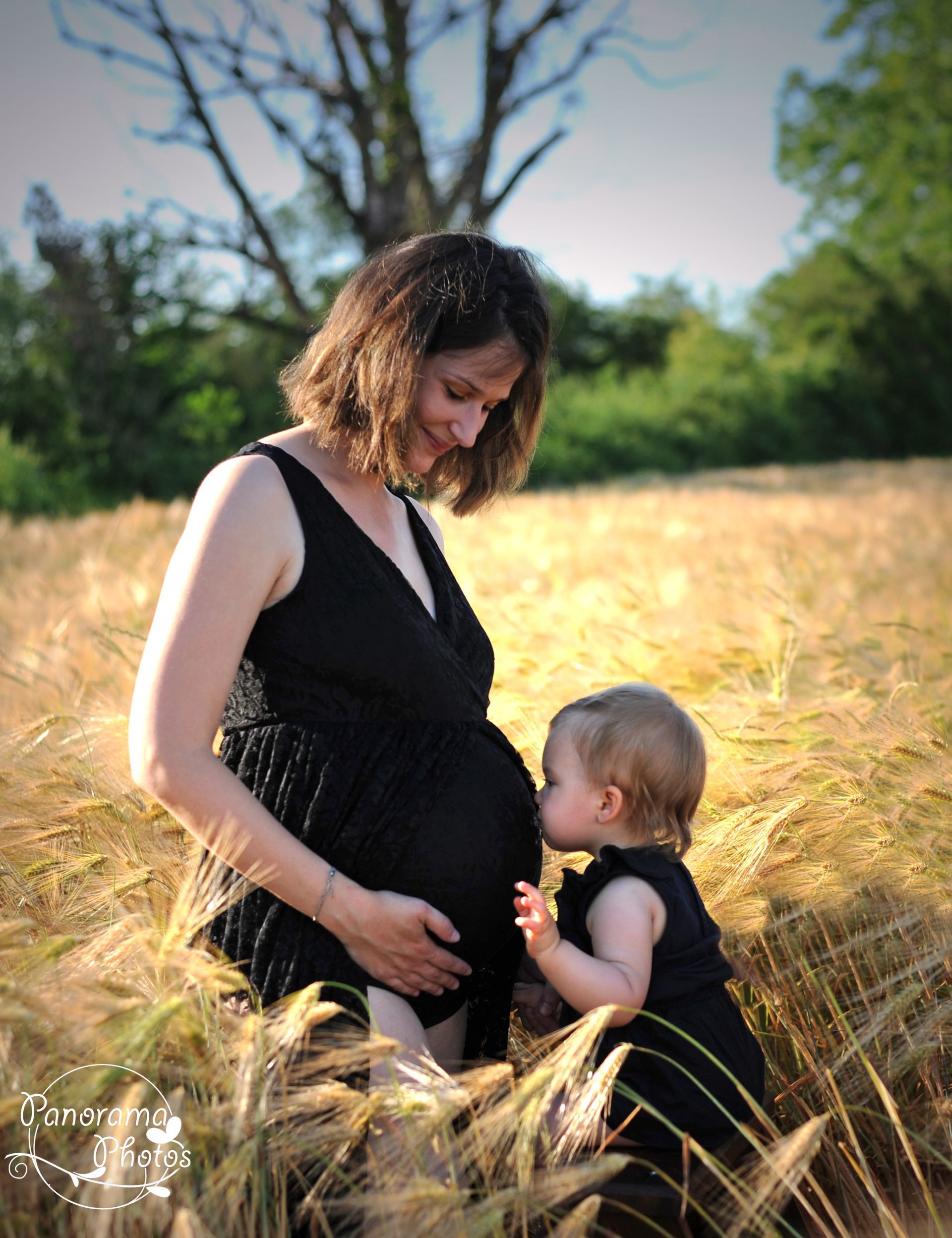 séance photo extérieure petite fille qui embrasse le ventre de sa maman enceinte dans un champs de blé