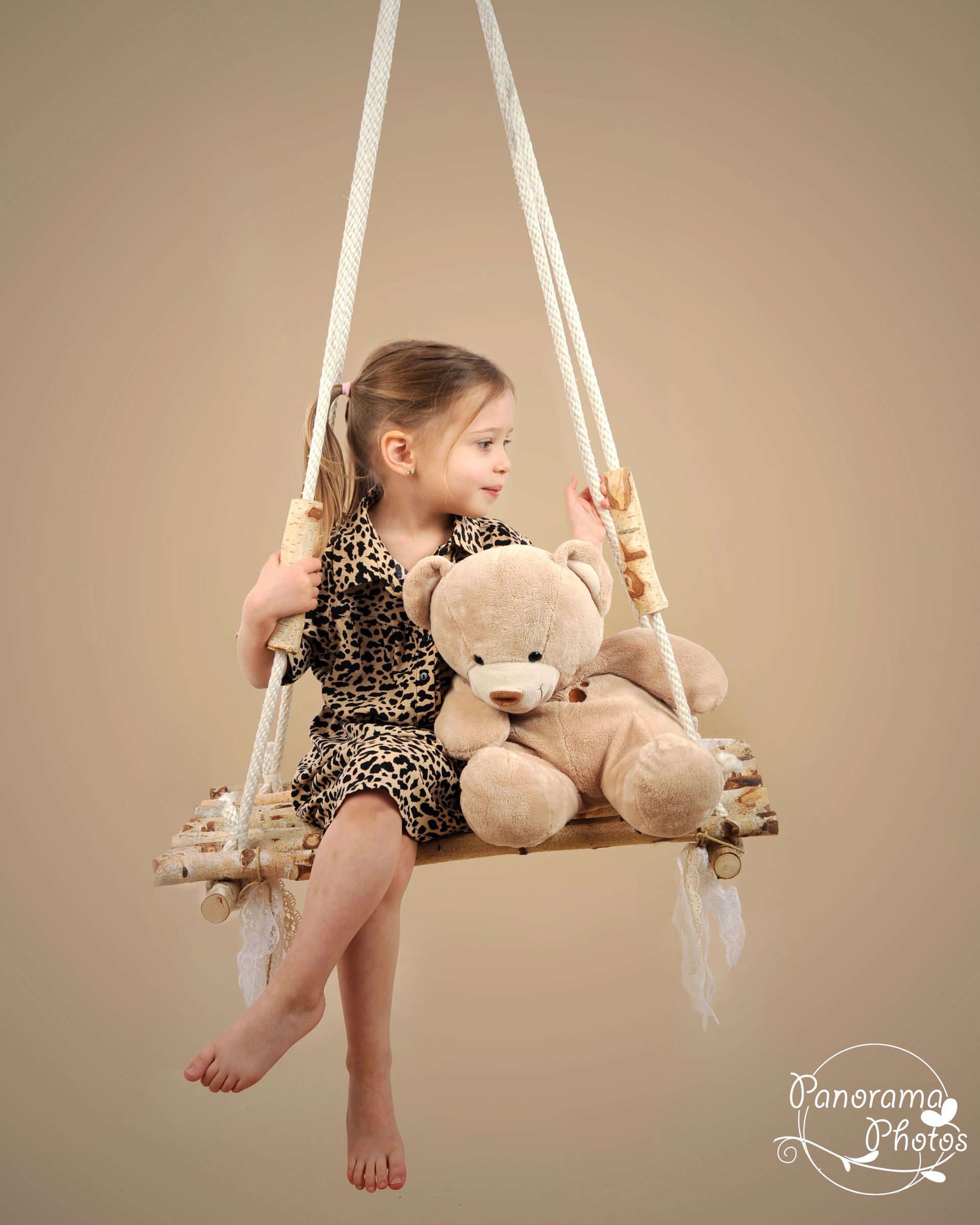 Portrait d'une petite fille sur une balançoire en bois avec son ours en peluche