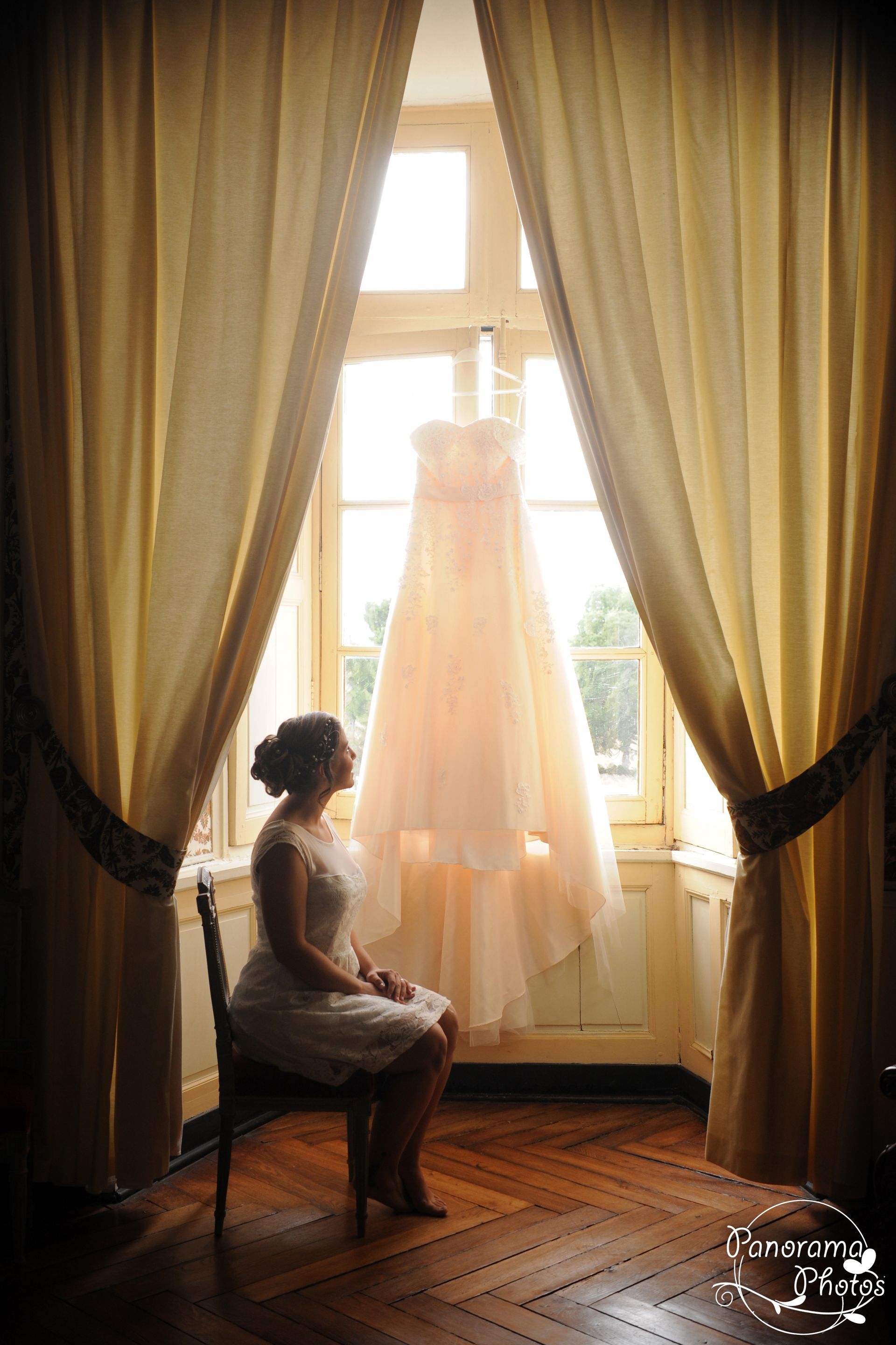 photo de mariage montrant une mariée assise devant une fenêtre regardant sa robe