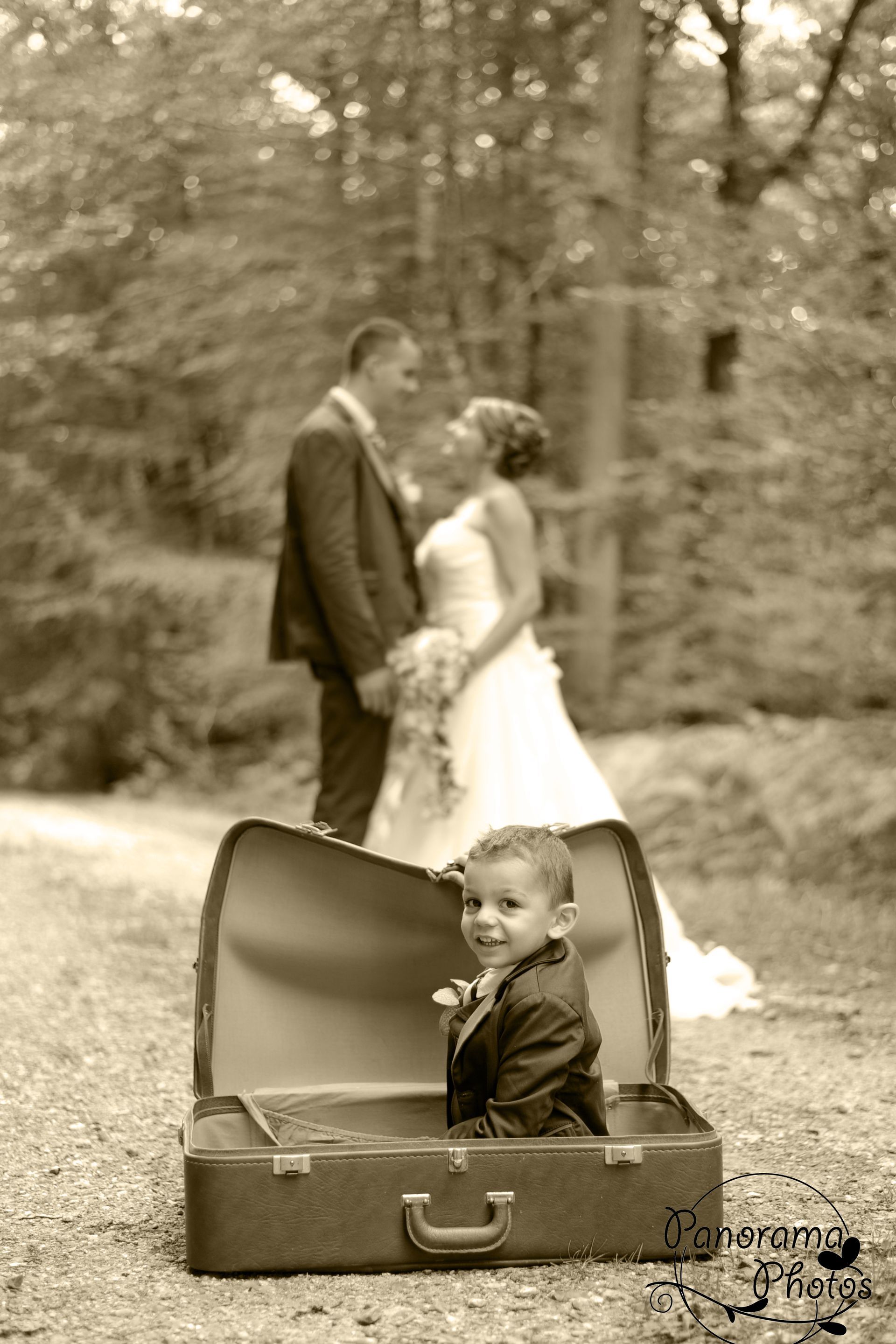 photo de mariage montrant un enfant assis dans une valise devant les mariés