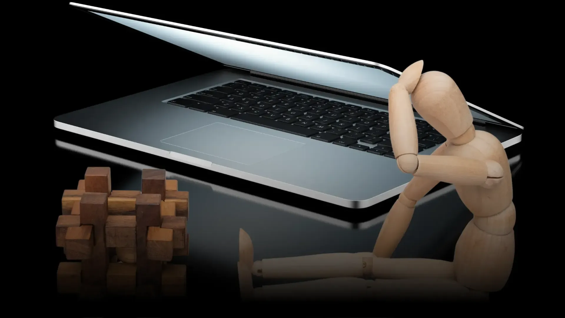 Zeichenpuppe aus Holz sitzt vor einem Holzwürfel-Rätsel; im Hintergrund ist ein Laptop zu sehen