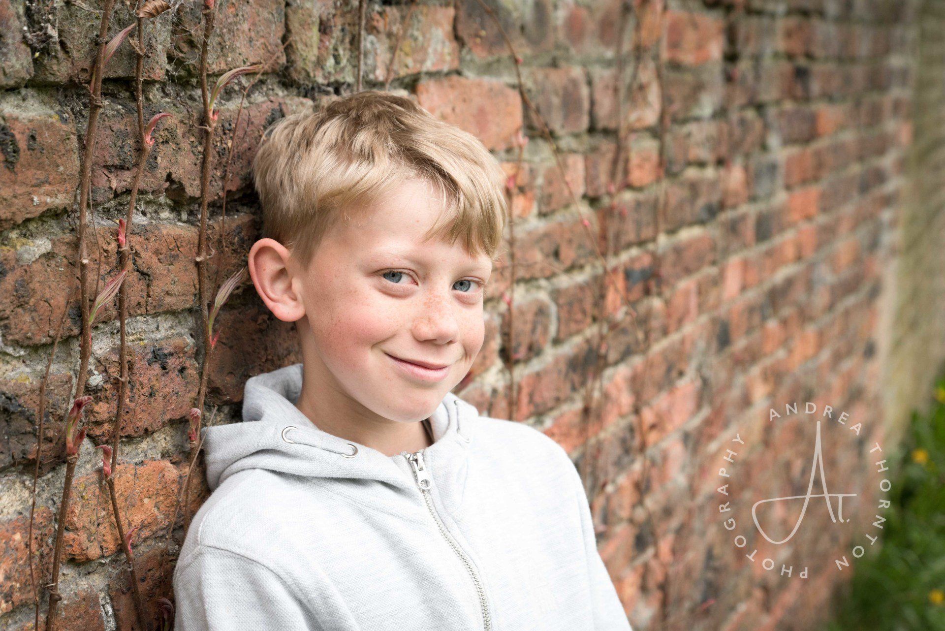 Smiling boy looking to camera leaning against a brick wall