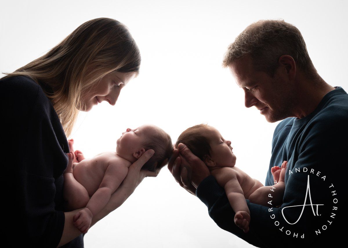 Parents facing each other holding their newborn twin babies