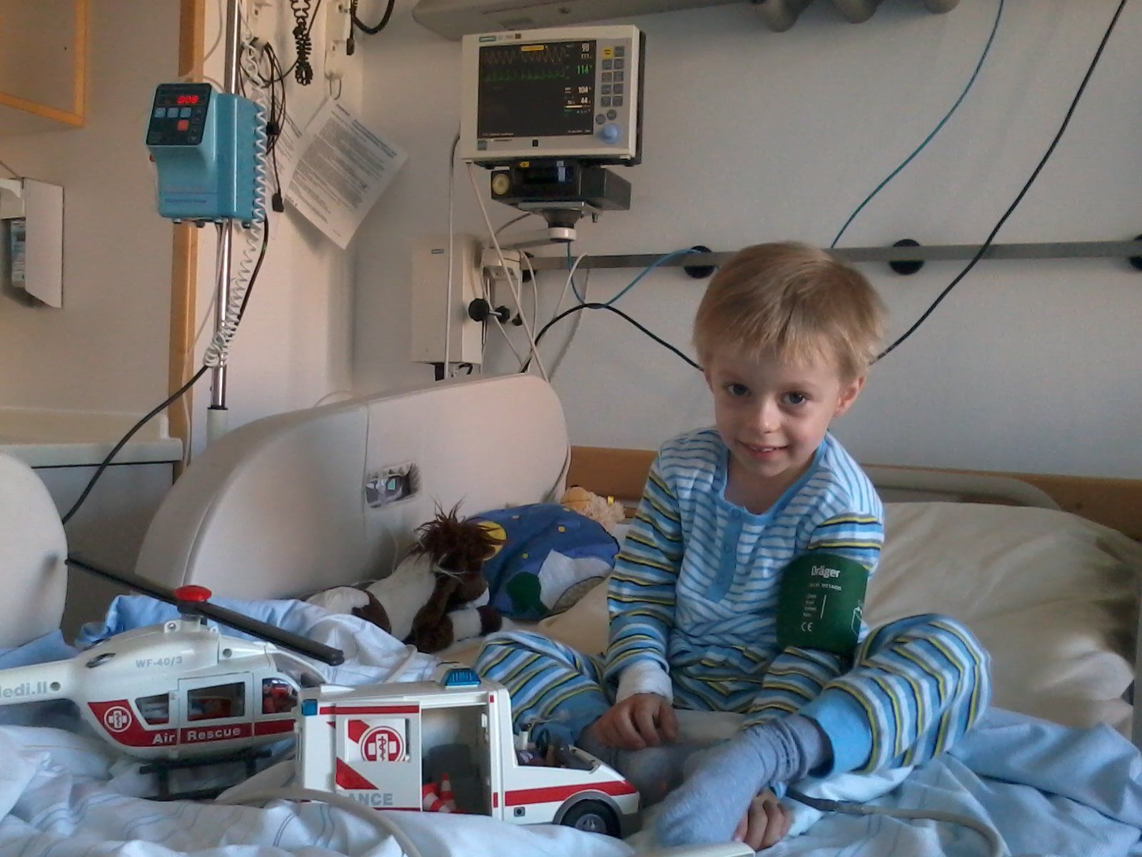 Kleiner Junge im gestreiften Schlafanzug sitzt auf einem Krankenhausbett.