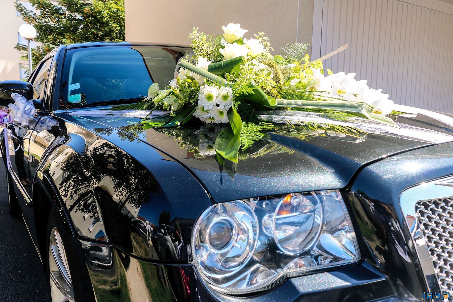 Gros plan sur un bouquet de fleurs de mariage (roses blanches et orchidées) ornant le capot d'une Chrysler 300C noire, détails de la décoration de la voiture du cortège.