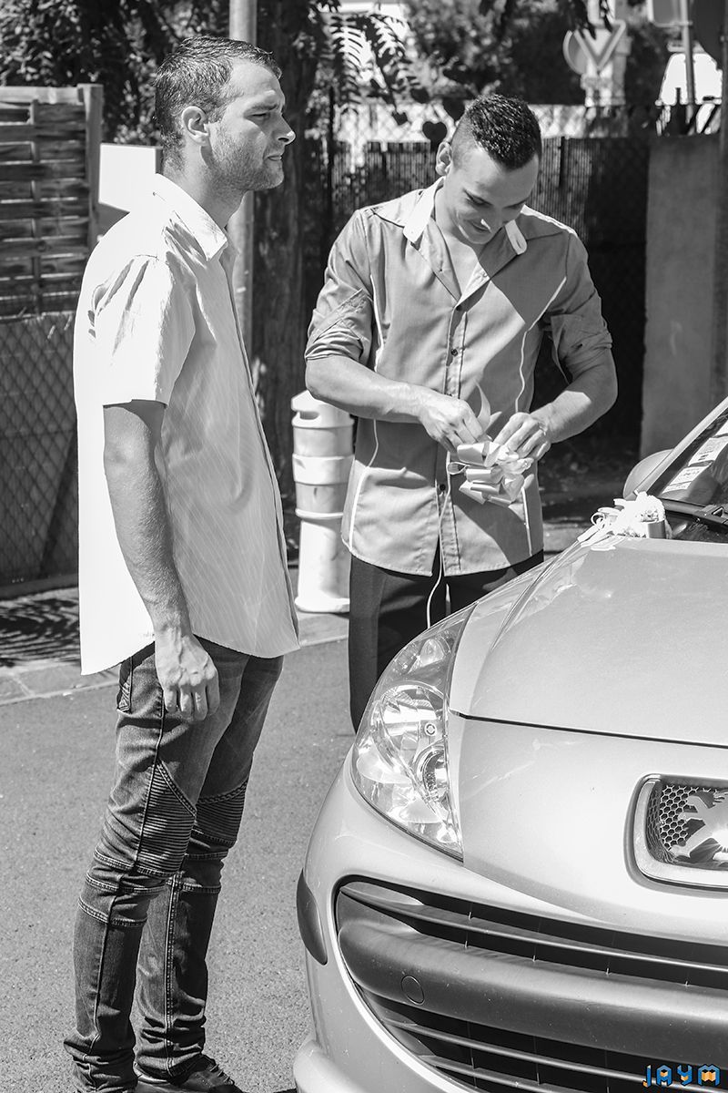 Avec Xavier Sanchez : deux hommes préparant et fixant un nœud de décoration sur la calandre d'une Peugeot 207.