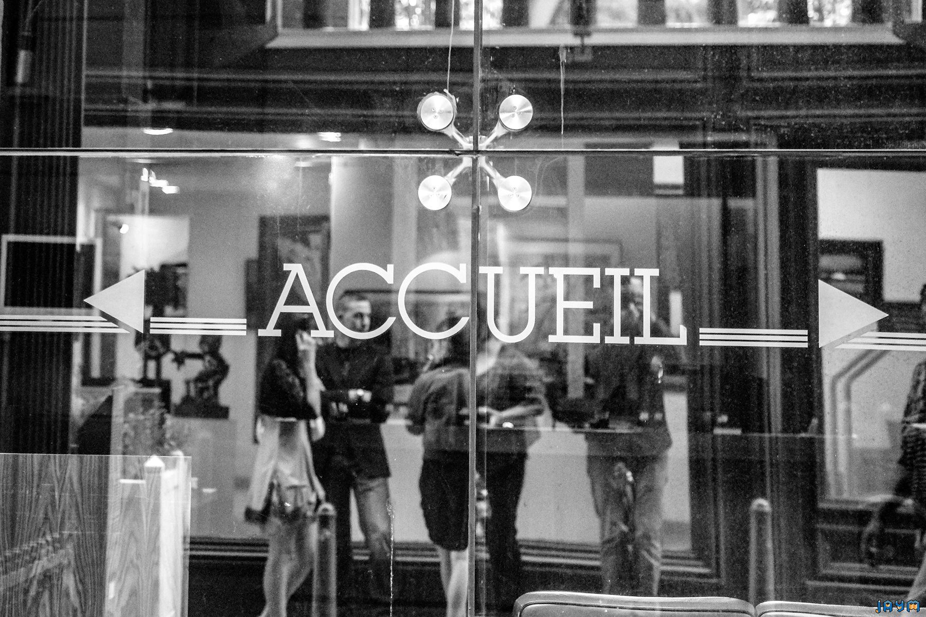 Vue à travers la vitrine d'un espace d'accueil événementiel à Clermont-Ferrand. Les reflets et le lettrage élégant annoncent une réception conviviale. Un cliché en noir et blanc capturant les premiers instants d'une cérémonie officielle.