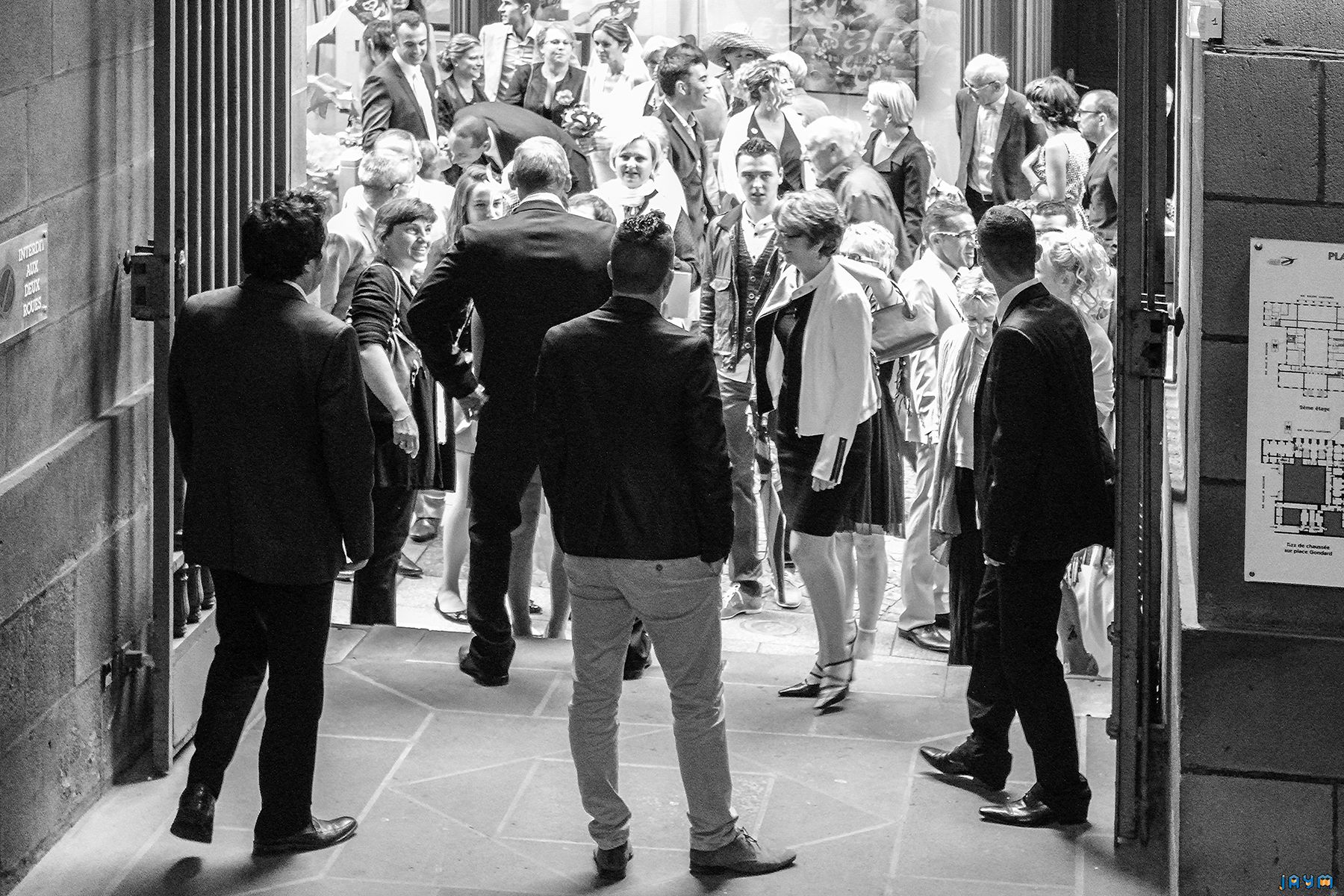 Vue en perspective de l'entrée des invités dans la salle de réception. Cette composition graphique en noir et blanc met en scène le flux des convives et l'architecture du lieu. Un moment clé de la journée de mariage de Clémentine et Nicolas, capturé avec élégance dans le centre de Clermont-Ferrand.