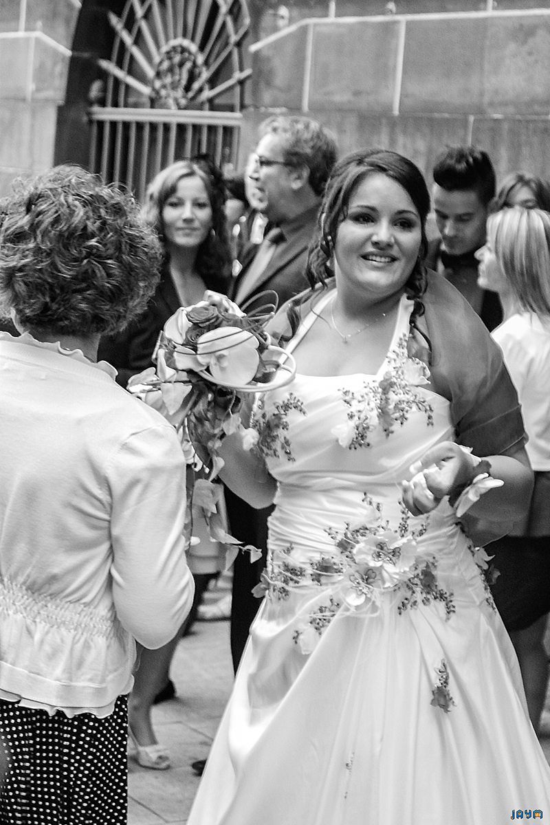 Portrait en noir et blanc saisissant de la mariée, radieuse et souriante. Ce cliché met en lumière la beauté de son expression et les détails raffinés de sa robe de mariage brodée de fleurs. Capturé sur le vif lors du rassemblement devant la mairie, ce portrait incarne l'émotion pure et l'élégance intemporelle d'une photographie de mariage professionnelle.