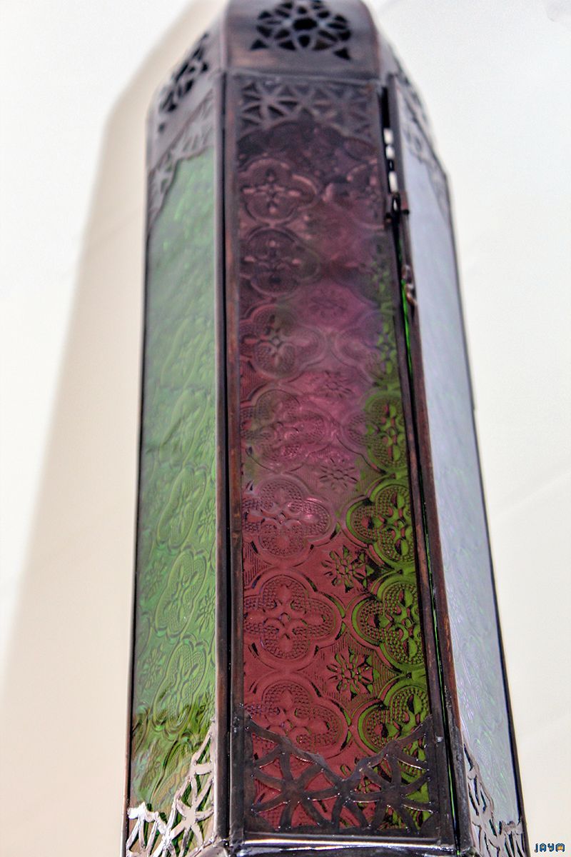 Détail d'une haute lanterne orientale avec des panneaux de verre texturés vert émeraude et rose fuchsia, reflétant la lumière.