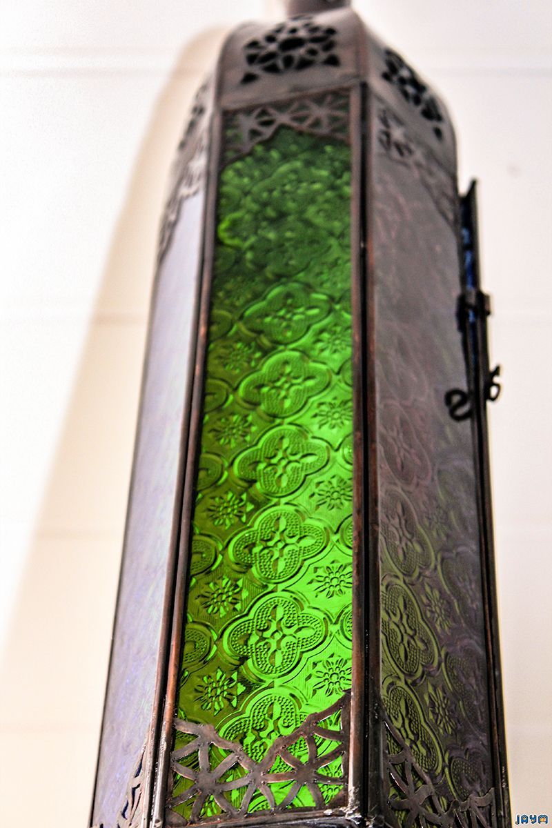 Focus sur la partie centrale d'une lanterne en métal, mettant en avant le verre vert vif aux motifs géométriques et floraux en relief.